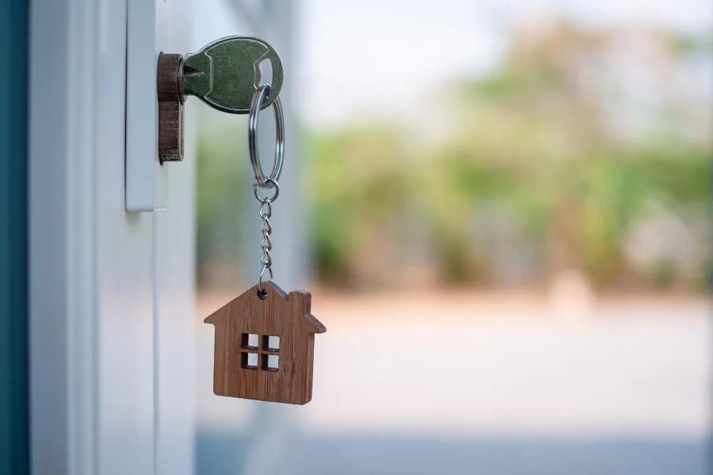 Key with house keychain hanging off of door to home.