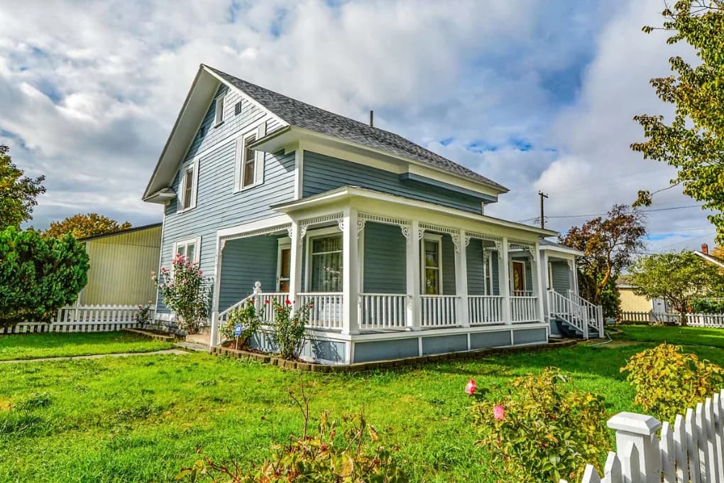 Street view of large blue house with spacious porch.