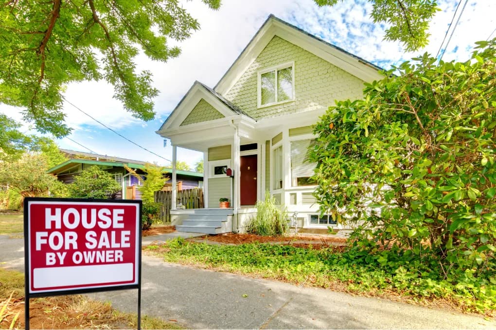 House with a "house for sale by owner" sign in front yard.