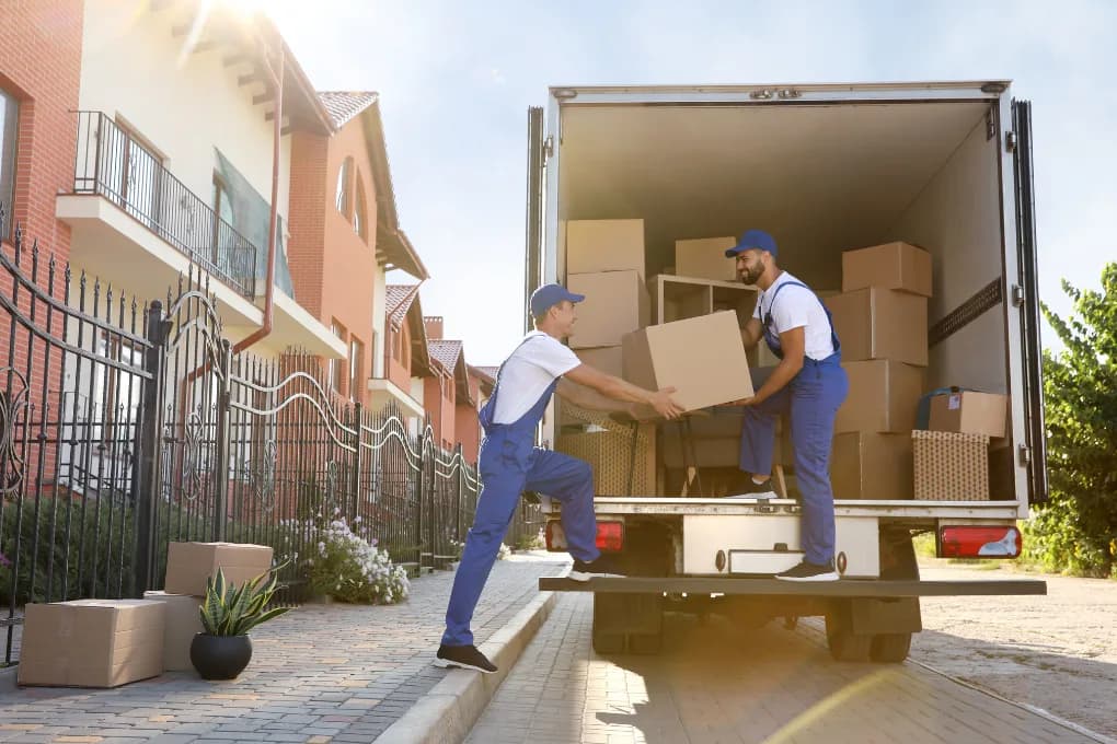 Two movers moving boxes out of truck into house.