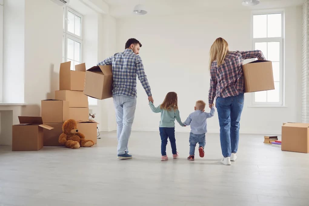 Family holding hands in new house with moving boxes around them.