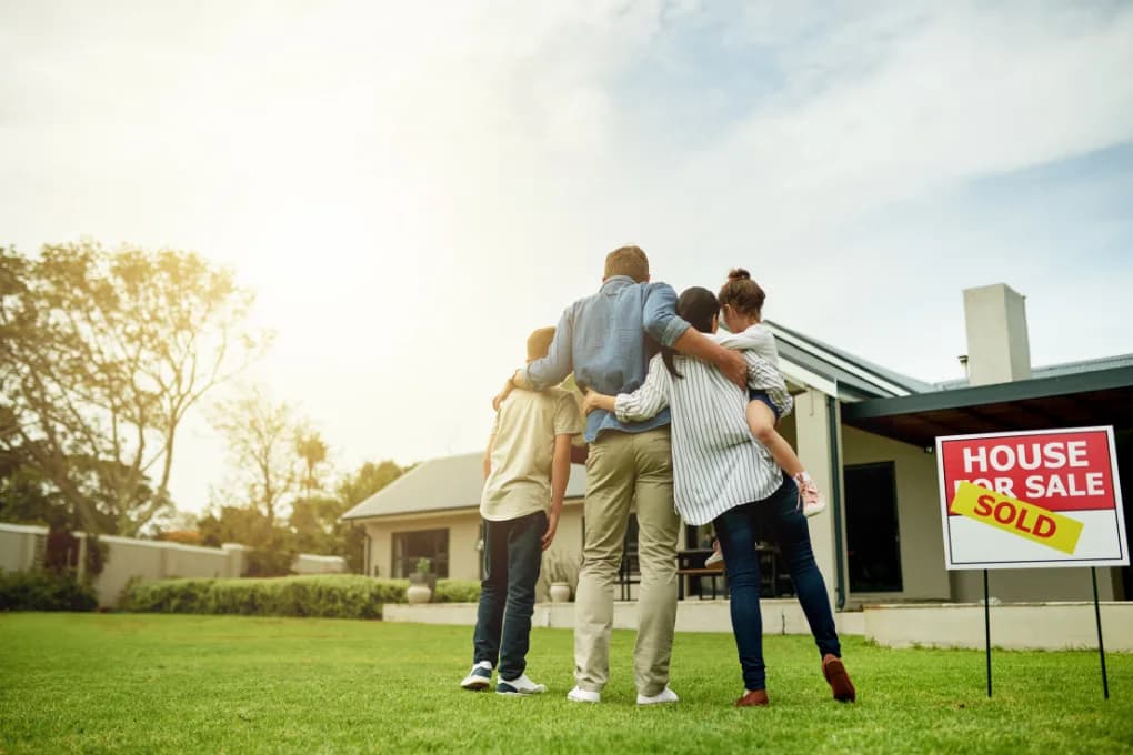 Family standing on yard in front of house with a sold sign next to them.