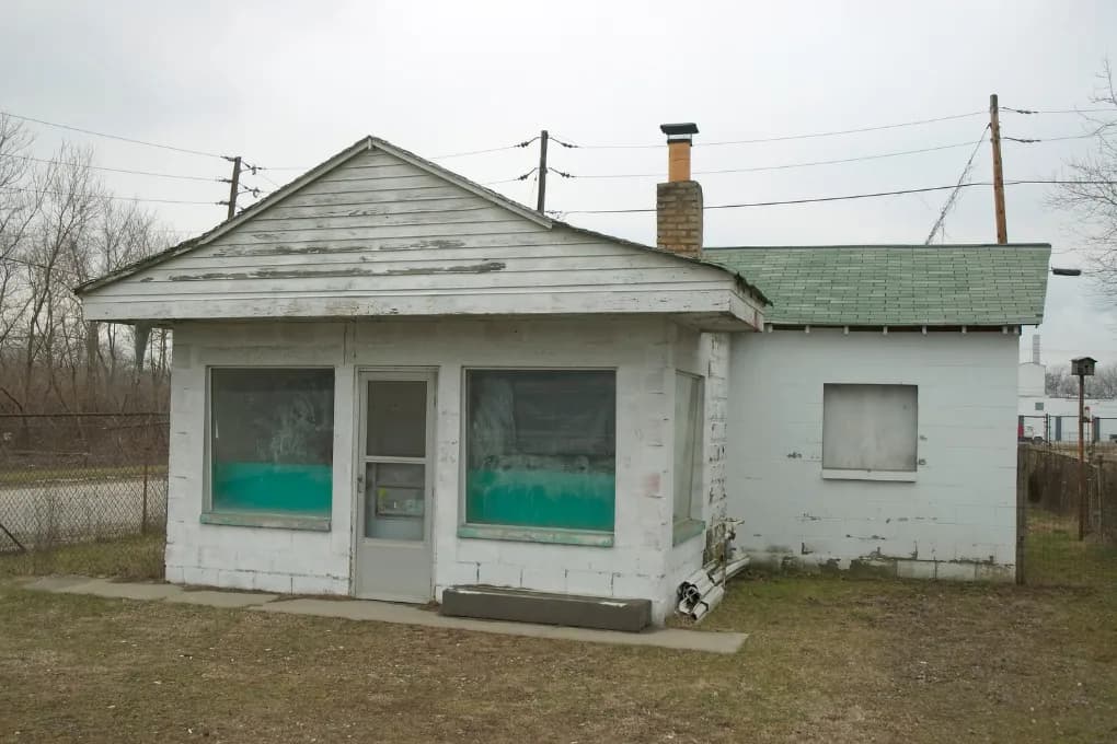 Street view of white house in need of repairs.
