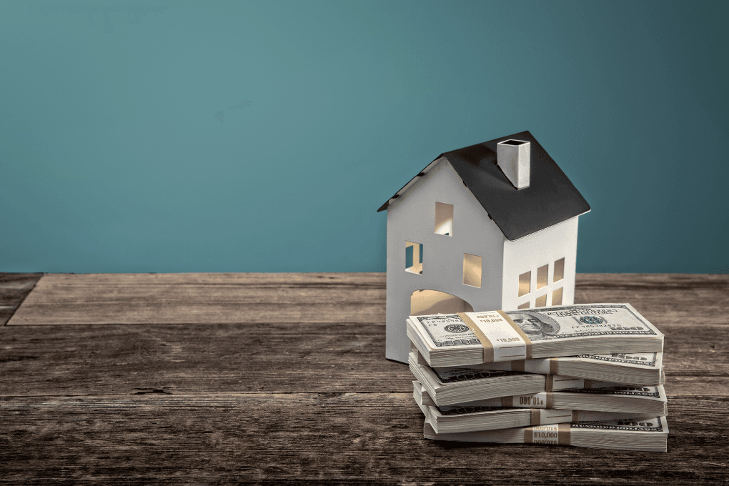 Toy house and stack of cash sitting on a table.