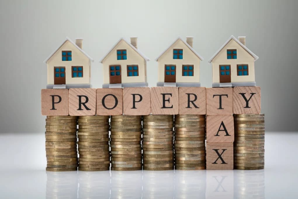Toy houses on top of stacks of coins with blocks that read property tax.